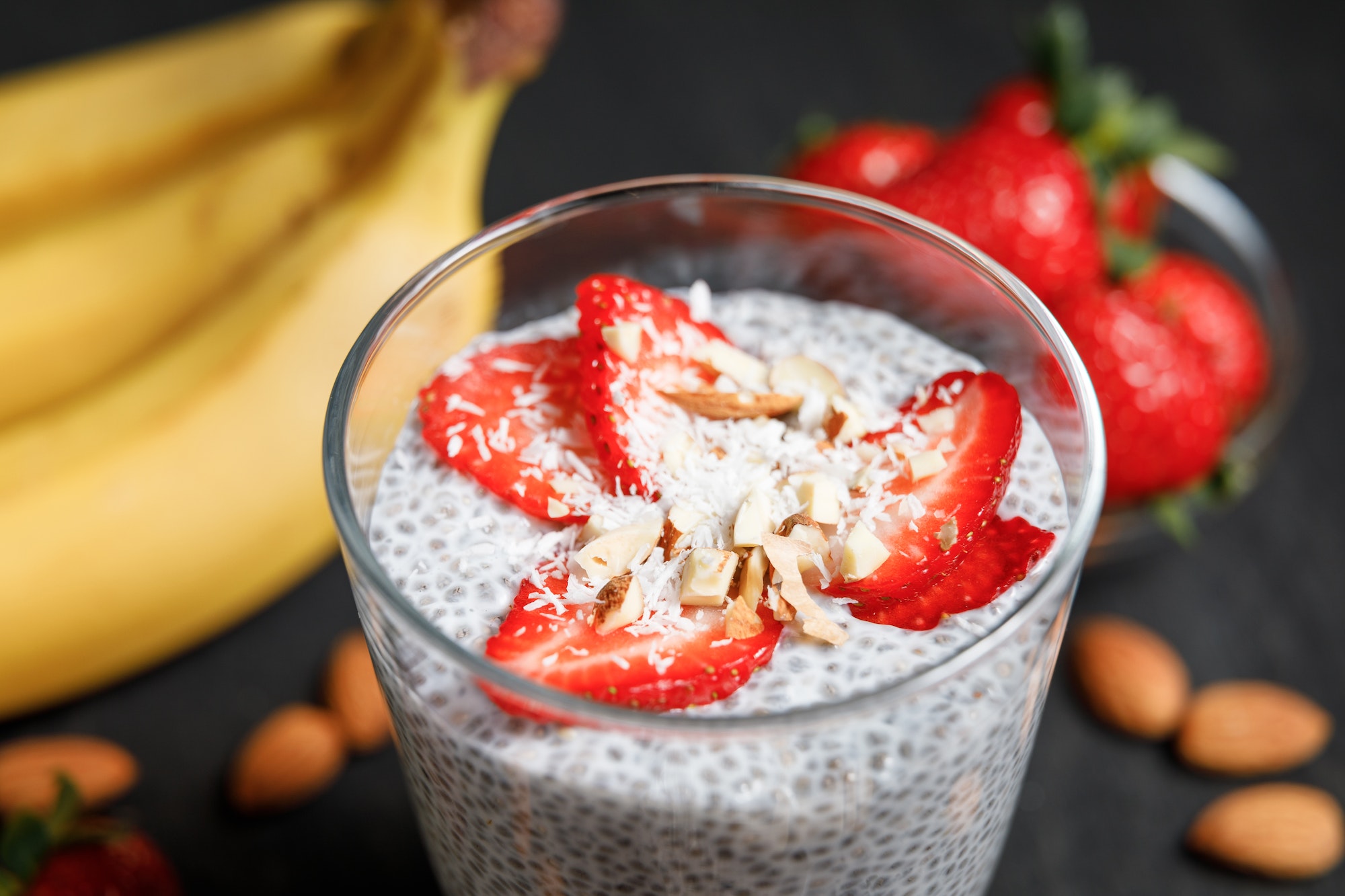 Chia seeds pudding with strawberries and coconut chips in glass on dark background.